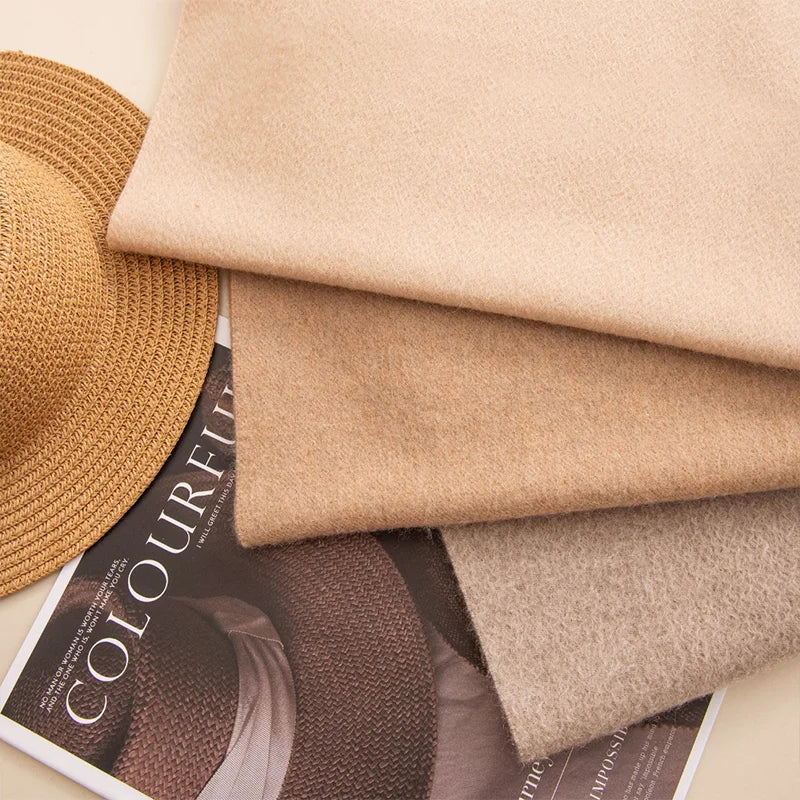 Cream camel and taupe scarves layered beside straw hat