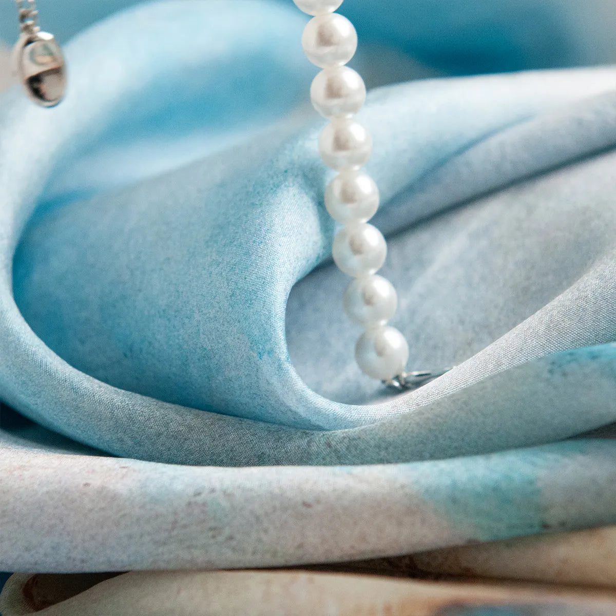 Folded azure silk scarf with pearl necklace