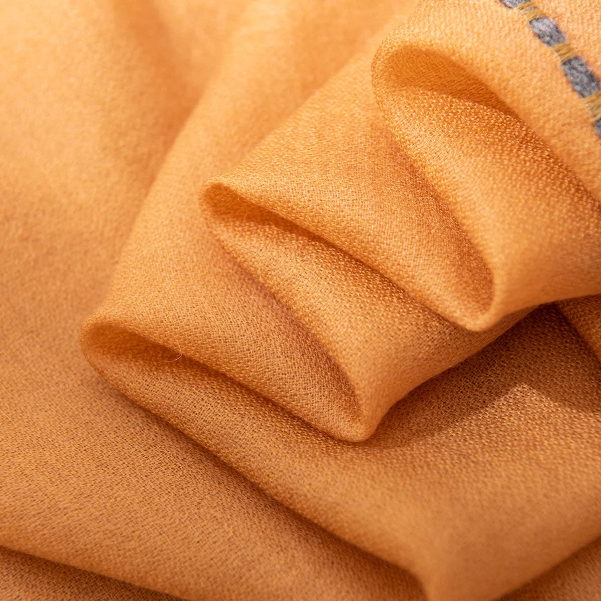Folded mustard wool scarf layers showing the fine woven surface