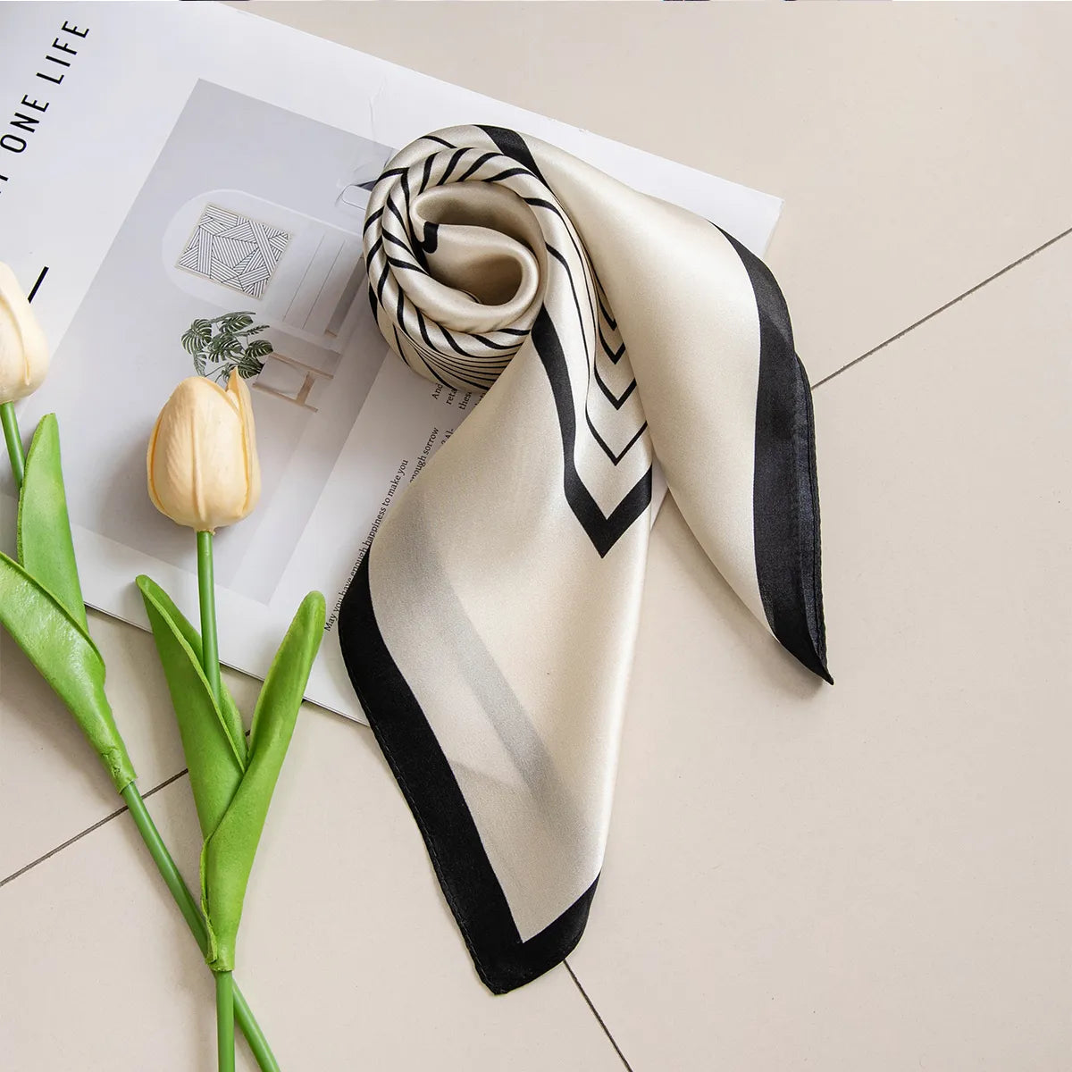 Rolled black-bordered silk scarf on a book with tulips