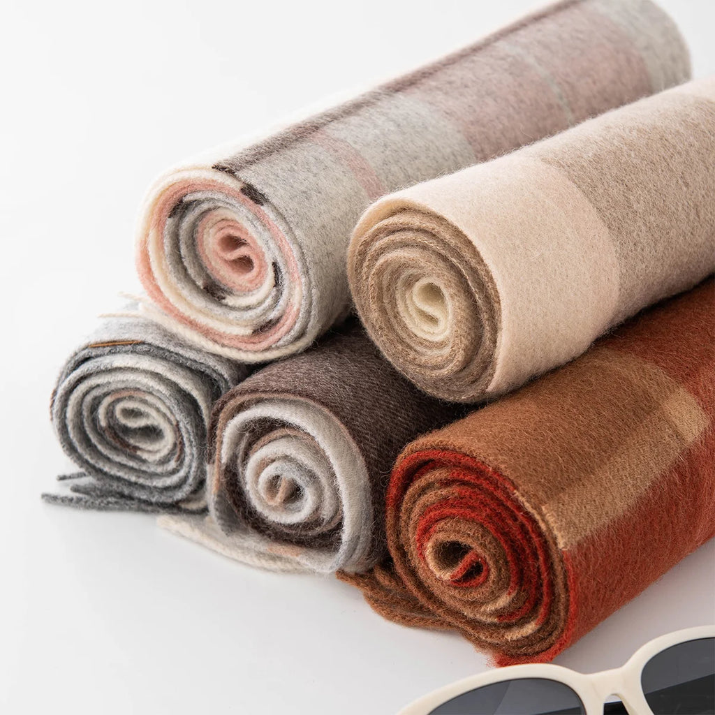 Rolled checked wool scarves displaying neutral gray and rust shades