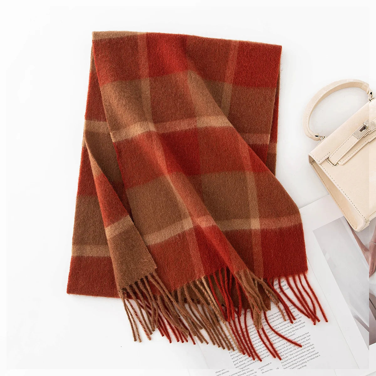 Rust red checked wool scarf folded beside a cream handbag